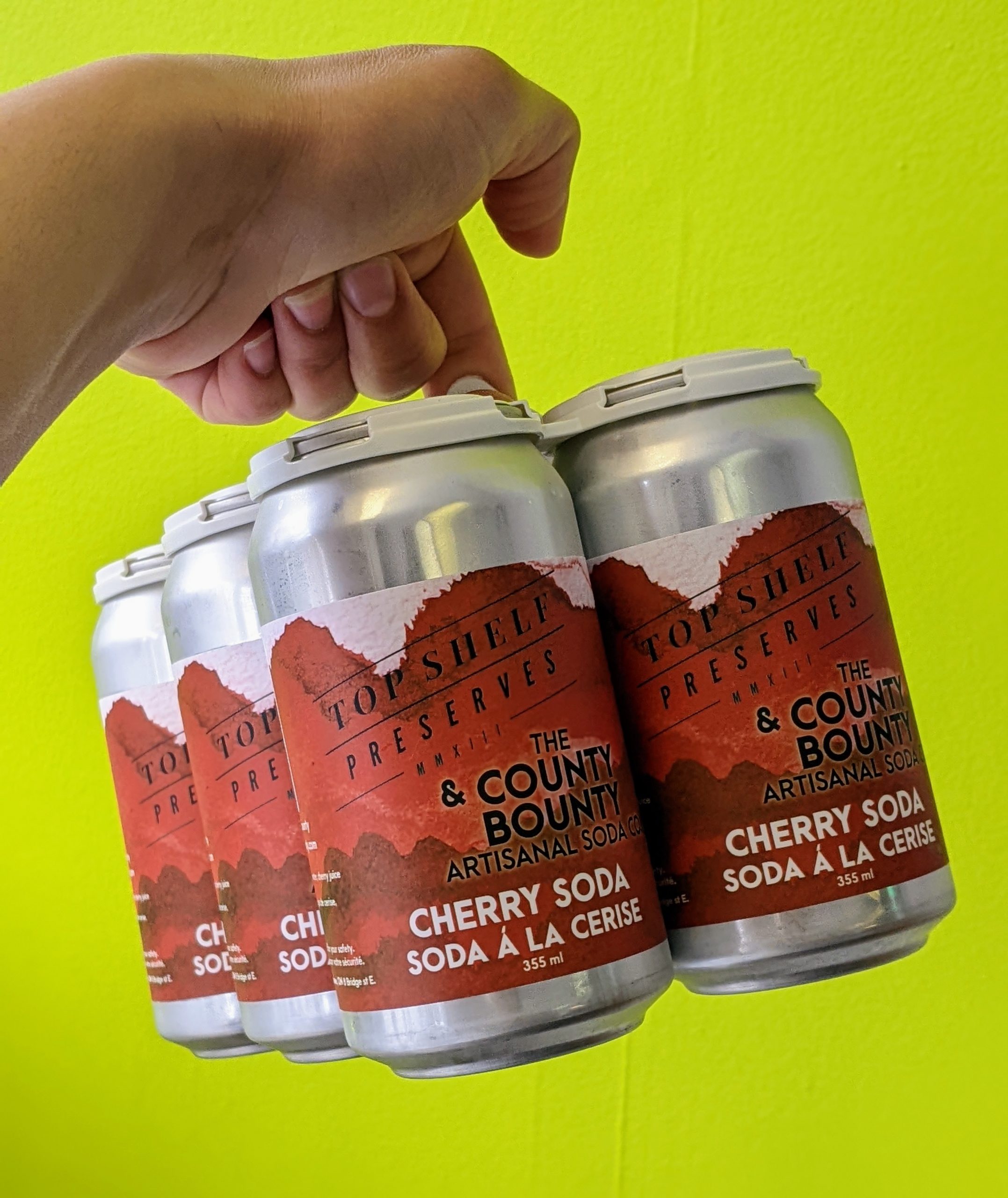 six cans of soda with a red label on a neon green background